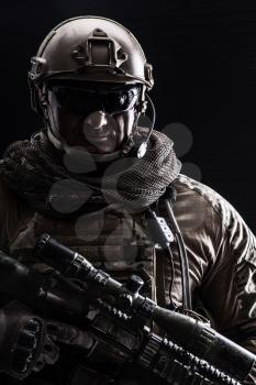 Studio contour backlight shot of special forces soldier in uniforms with weapons, portrait on black background