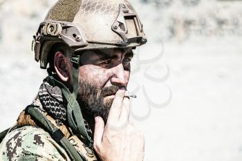 Closeup shot of smoking soldier in the desert among rocks