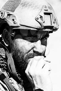 Closeup black and white shot of smoking soldier in the desert among rocks