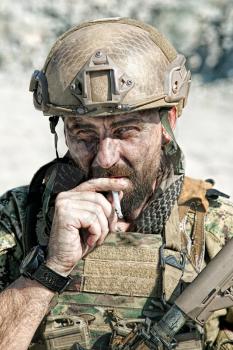 Closeup shot of smoking soldier in the desert among rocks