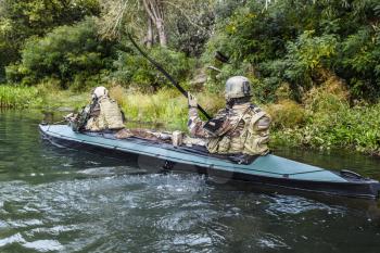 Special forces men with painted faces in camouflage uniforms paddling army kayak. Boat moving across the river, diversionary mission, back view