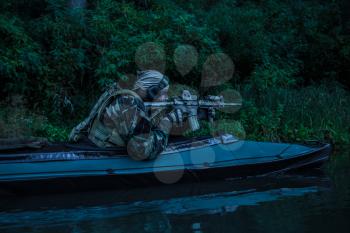 Special forces man with painted face in camouflage uniforms in army kayak. Seeking target, diversionary mission, twilight