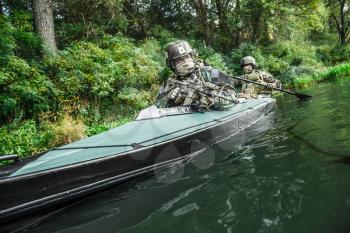 Special forces men with painted faces in camouflage uniforms paddling army kayak. Boat moving across the river, diversionary mission, diagonal view
