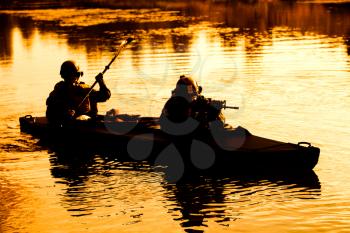 Silhouette of special forces men paddling army kayak. Boat moving calmly across the river, diversionary mission, sunset dusk