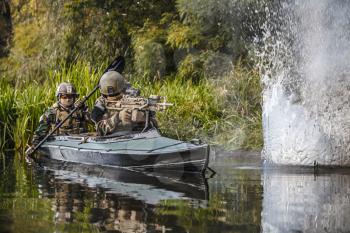 Special forces men with painted faces in camouflage uniforms paddling army kayak. Sudden nearby bomb explosion, water blast