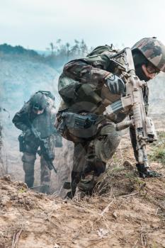 Two french paratroopers of 1st Marine Infantry Parachute Regiment RPIMA, in action jumping out of enemy trench filled with gunpowder smoke
