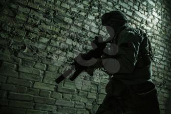 Special forces operator pointing weapon in the dark. Combat helmet, and bulletproof vest are on. Low key image, shadow soldier