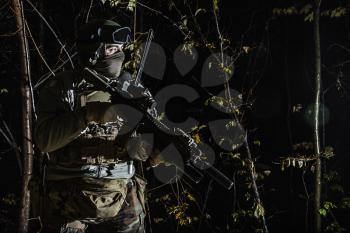 Marine Special Operator also known as Marsoc raider with weapons in greenery at nighttime turning looking away. Caucasian, profile view, half length