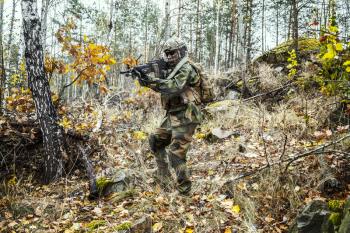 Norwegian Rapid reaction special forces FSK soldier patrolling in the forest. Field camo uniforms, knee pads, combat helmet and eye-wear goggles are on