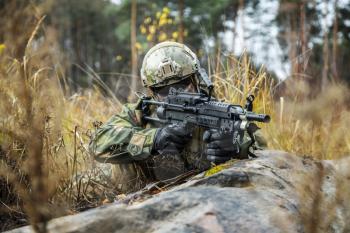 Norwegian Rapid reaction special forces FSK soldier firing in the forest. Field camo uniforms, combat helmet and eye-wear goggles are on