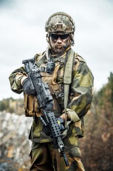 Norwegian Rapid reaction special forces FSK soldier patrolling in the forest. Painted face, combat helmet and eye-wear goggles are on