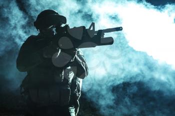 Black silhouette of soldier with grenade launcher in the smoke moving in battle operation. Back light, cropped, toned and colorized