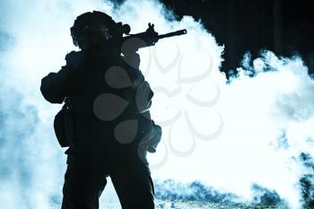 Black silhouette of soldier in the smoke moving in battle operation. Back light, cropped, toned and colorized