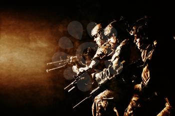 Group of security forces in Combat Uniforms with rifles, lined in the face of danger. Facing enemy, they stand boldly and ready to protect the nation. Studio contour silhouette shot, backlight, profile side view