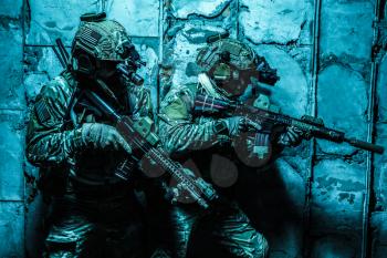 Squad of Army Rangers moving along the concrete wall on mission. They are ready to contact with enemy and to kill. Outdoor location shot, darkness of night, dim light