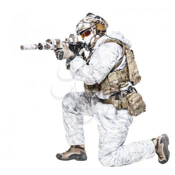 Special forces operator of Navy Seals armed with assault rifle with closed face in polarized sunglasses and military winter camo clothes shooting in kneeling position. Studio shot