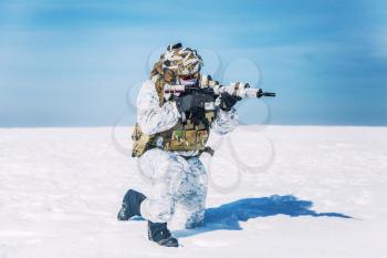 Army soldier with weapon in the Arctic. He wears chest rig, backpack, suffers from extreme cold, strong wind, but endures while mission continues, killing in snow desert. Shooting in kneeling position