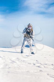 Army serviceman in winter camo somewhere in the Arctic. He wears chest rig, backpack, suffers from extreme cold, strong wind, but endures while mission continues, running moving across snow desert