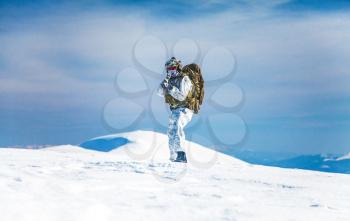Army serviceman in winter camo somewhere in the Arctic. He wears chest rig and huge backpack, suffers from the extreme cold and strong wind, but endures while mission continues. Blue sky background