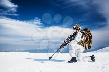 Army soldier with Sniper rifle in action in the Arctic. He wears chest rig, backpack, suffers from extreme cold, strong wind, but endures while mission continues, in snow desert