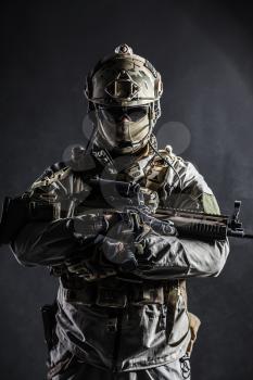 Army soldier in Protective Combat Uniform holding Special Operations Forces Combat Assault Rifle. Studio shot, dark contrast, cropped, black dark background