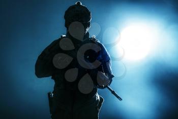 Army soldier in Protective Combat Uniform holding Special Operations Forces Combat Assault Rifle. Studio shot, backlit silhouette