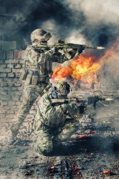 Pair of special forces shooting a weapons. Brothers in arms in action. Guns blazing, ruined walls of buildings, explosions, gunfire and smoke on background