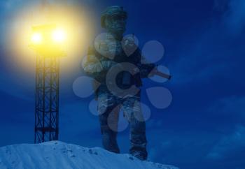 US Military security service serviceman in camo uniform, helmet and mask, armed with assault rifle standing in backlight beam of war watchtower search light. Military base or prison night watch guard