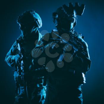 Two members of army elite forces, counter terrorism squad soldiers in battle uniform with modern tactical ammunition, armed service rifles, standing together shoulder to shoulder, low key studio shoot