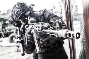 Army special forces shooter, police anti-terrorist squad fighter, private security company guard in tactical ammunition aiming with service rifle. Police raid, counter-terrorist operation, desaturated