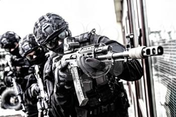 Army special forces shooter, police anti-terrorist squad fighter, private security company guard in tactical ammunition aiming with service rifle. Police raid, counter-terrorist operation, desaturated