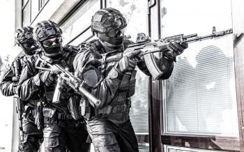 Police counter terrorist tactical unit, special reaction team in black blank uniforms with hidden identity, armed with assault rifles, moving in stack formation during terrorism response operation