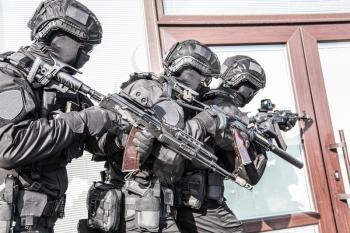 Police counter terrorist tactical unit, special reaction team in black blank uniforms with hidden identity, armed with assault rifles, moving in stack formation during terrorism response operation