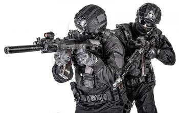 Two SWAT fighters, police special operations tactical group members in black uniform ans helmet, armed with assault rifles moving forward one behind another studio shoot isolated on white background