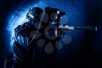 Police special operations team, quick response group fighter in black uniform, helmet and mask aiming with pistol equipped silencer while hiding behind ballistic shield, toned, low key studio shoot