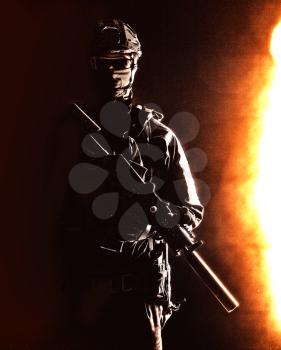 Portrait of modern infantry soldier, special operations forces rifleman, police tactical group fighter in helmet and mask armed with silenced service rifle, low key with hard side light studio shoot