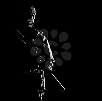 Portrait of modern infantry soldier, special operations forces rifleman, police tactical group fighter in helmet and mask armed with silenced service rifle, low key with hard side light studio shoot