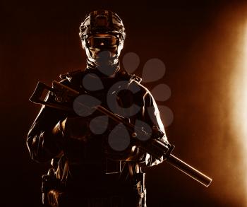 Half-length portrait of special forces soldier, army commando, police tactical team or SWAT fighter with hidden behind mask and glasses face, armed assault rifle with silencer, low key studio shoot