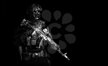 Police assault team member, special forces soldier, private security service, military company serviceman in black ammunition and uniform, armed service rifle, high contrast studio shoot on black