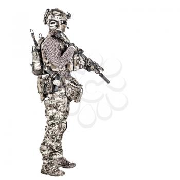 Full length portrait of airsoft player in checkered shirt, wearing camouflage uniform, helmet with tactical radio headset, body armour, aiming with service rifle replica studio shoot isolated on white