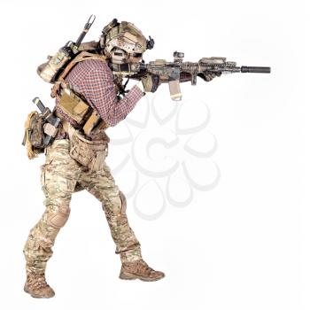 Full length portrait of airsoft player in checkered shirt, wearing camouflage uniform, helmet with tactical radio headset, body armour, aiming with service rifle replica studio shoot isolated on white