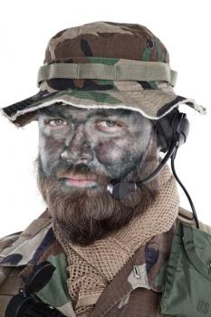 Shoulder studio portrait of commando soldier, modern mercenary, professional soldier with black camouflage paint on bearded face, tactical radio headset with microphone, isolated on white background