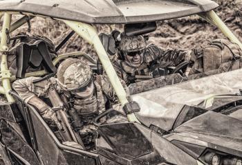 Armed modern infantry soldiers, elite members of special forces, private military company mercenaries extremely driving desert patrol vehicle while going at rough terrain. Desaturated, cropped shoot