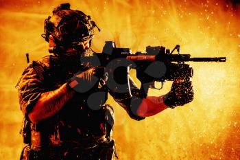 US army special forces shooter, modern combatant in battle helmet with radio headset, hiding face, aiming service rifle, fighting with enemies, shooting targets on fiery background with water droplets