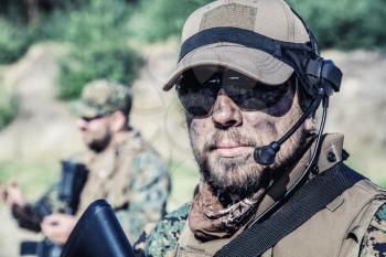 Location shot of United States Marine with rifle weapons in uniforms. Military equipment, army helmet, warpaint, smoked dirty face, tactical gloves. Weapons, army, patriotism concept