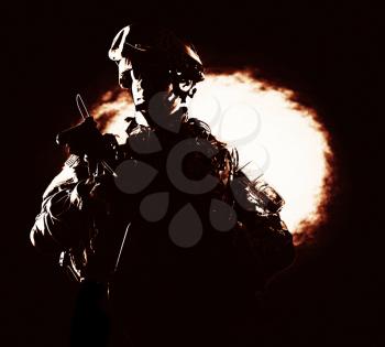 High contrast portrait of confident special operations forces soldier, armed and equipped, valiantly standing on black background with ball of fire. Heroic, brave veteran of war or military conflict