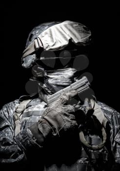 Special operations forces soldier in combat helmet with hidden behind balaclava and dark glasses face posing with sidearm service pistol in hand. Brown tone, high contrast, cropped on black background