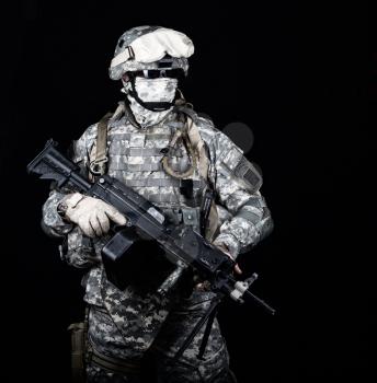 Marine with hiding identity, protected with helmet and body armour in digital camouflage combat uniform posing with light machine gun equipped infrared laser aiming light isolated on black background