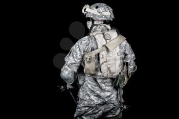 Back view of modern military forces infantry, US marine armed with rifle in digital camouflage combat uniform, protected helmet and body armour with hydration pack on back isolated on black background