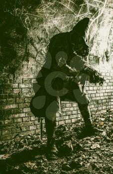 Post apocalyptic survivor, living underground mutant, wearing tattered rags hiding in deep bunker, city tunnel or catacombs, sneaking in dungeon with handmade firearm weapon, low key, toned image